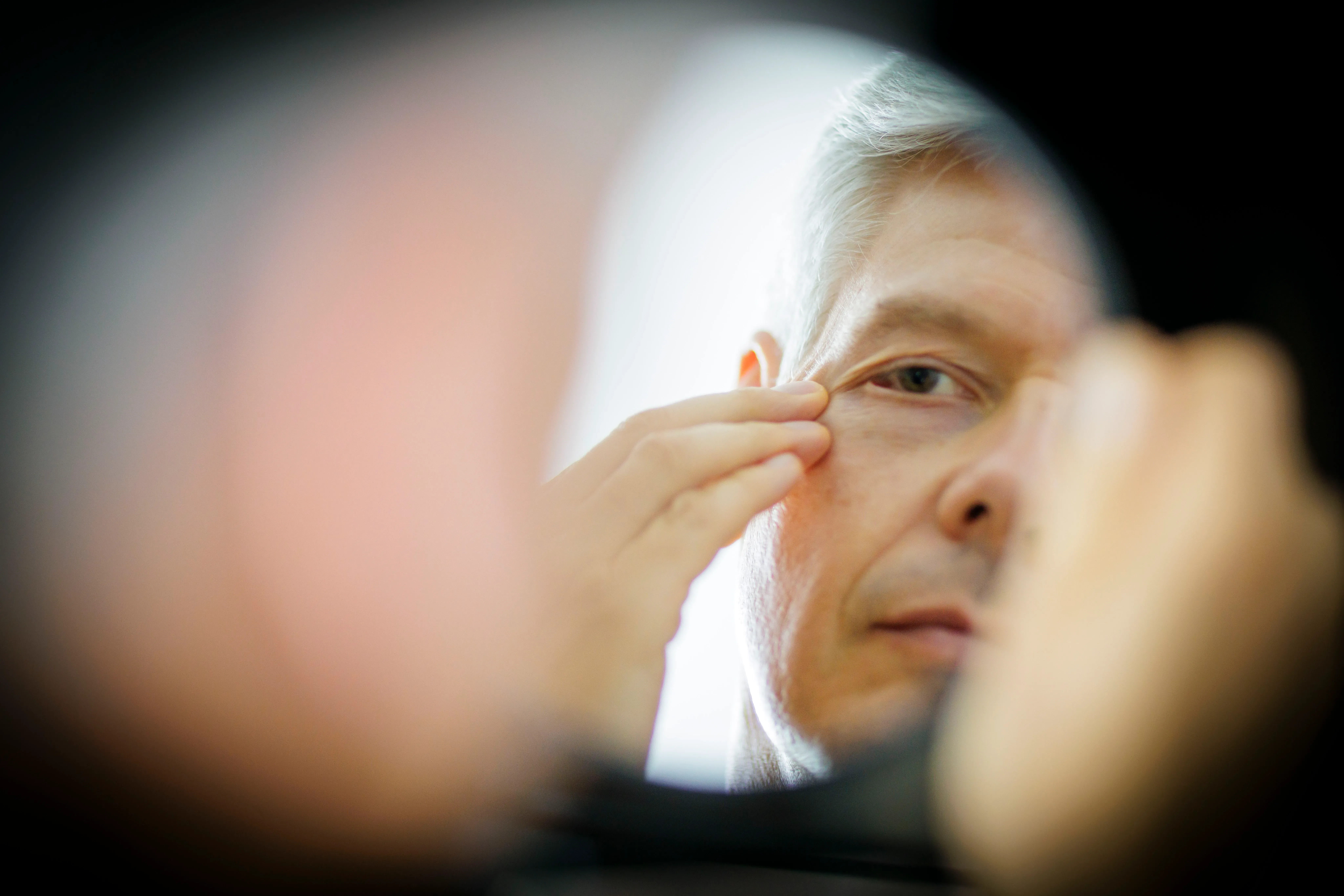 رجل في الخمسينات من عمره يتفحص علامات الشيخوخة حول عينيه في مرآة، مما يعكس تأثير المواد الكيميائية الأبدية على الشيخوخة.