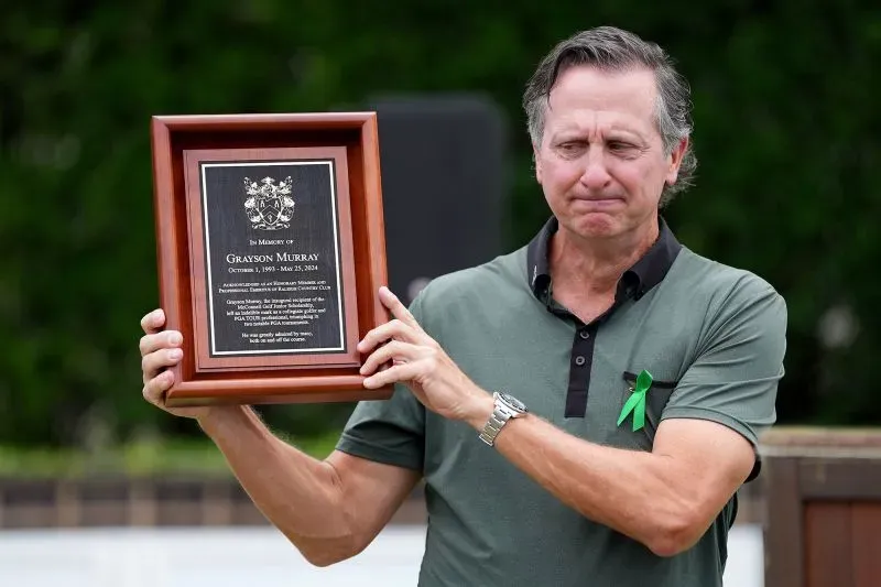 رجل يحمل لوحة تكريمية تحمل اسم غرايسون موراي، مع تعبير حزين على وجهه، في حدث يركز على الصحة العقلية للاعبين.