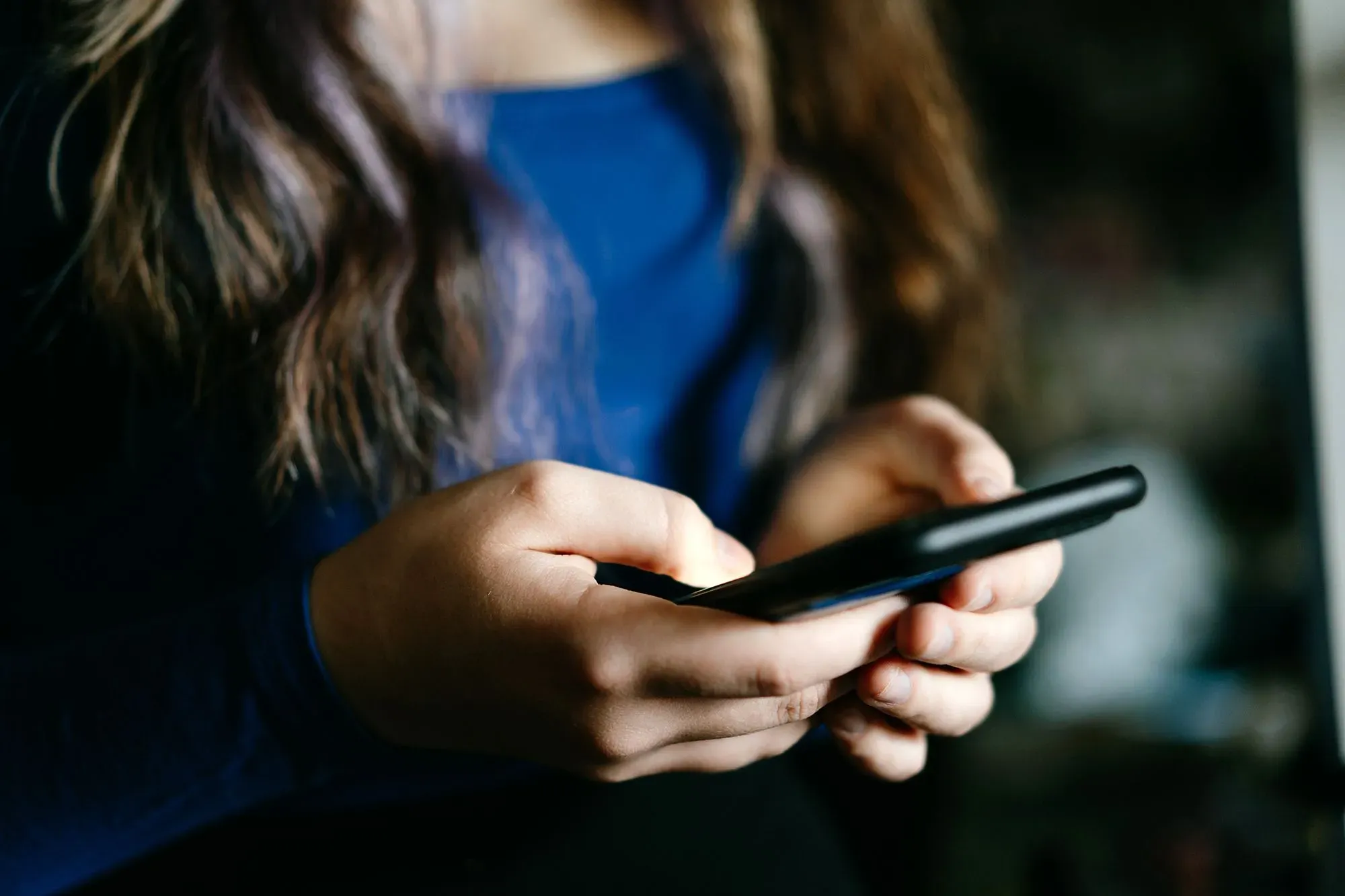 يد تظهر يد فتاة شابة تحمل هاتفًا ذكيًا، مما يعكس استخدام وسائل التواصل الاجتماعي وتأثيرها على الصحة العقلية للشباب.