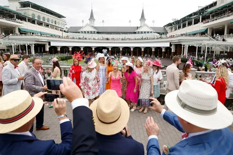 مجموعة من الأشخاص يرتدون أزياء ملونة وقبعات مزخرفة في مضمار تشرشل داونز خلال سباق كنتاكي ديربي، مع أجواء احتفالية مميزة.