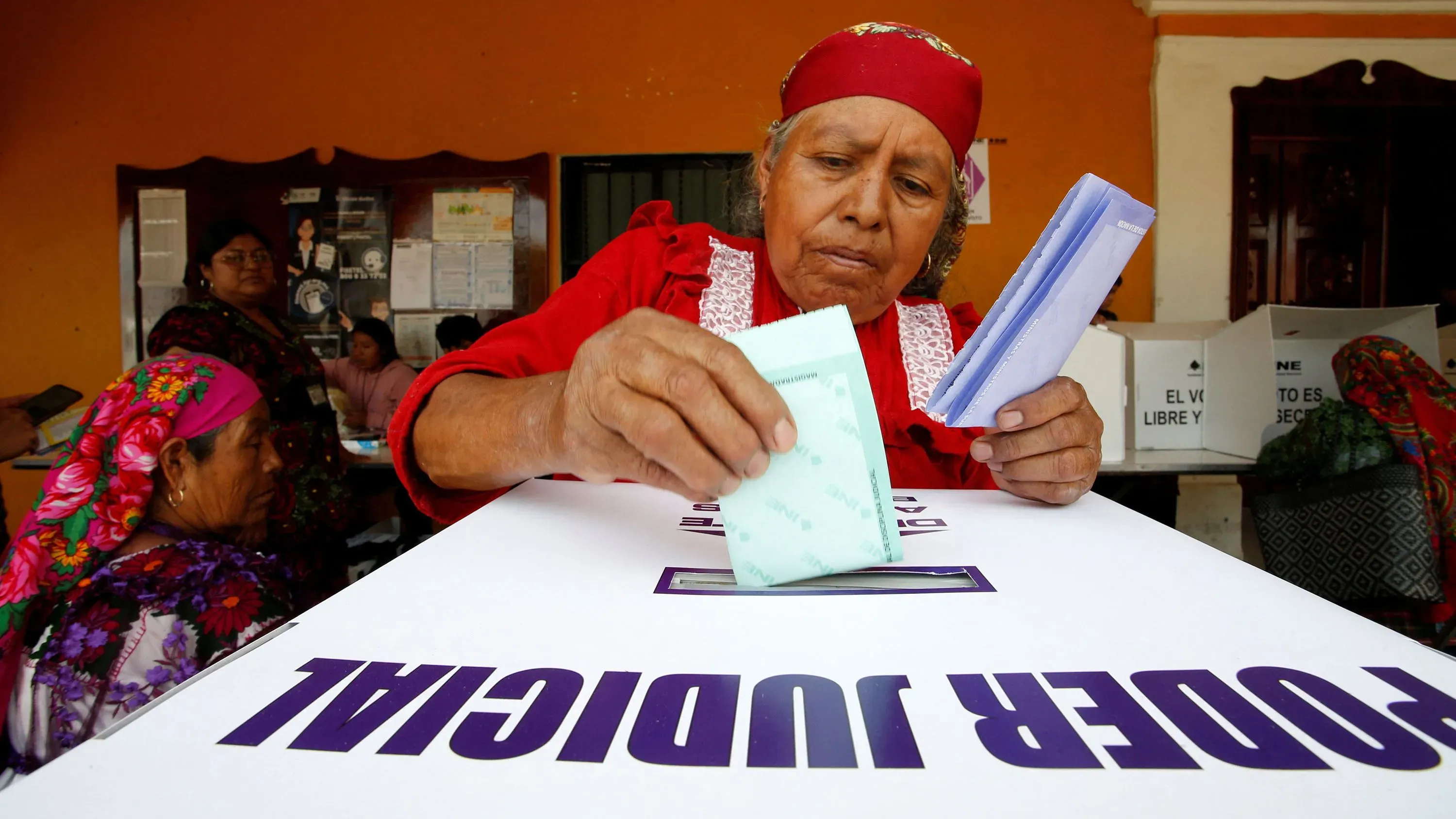 امرأة مسنّة ترتدي زيًا تقليديًا، تضع ورقة الاقتراع في صندوق الانتخاب خلال أول انتخابات قضائية في المكسيك. تعكس المشاركة الشعبية في العملية الديمقراطية.