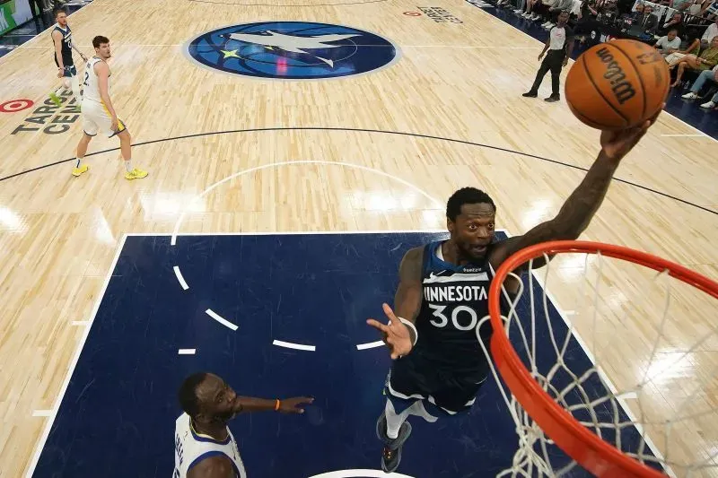 جوليوس راندل يقفز نحو السلة لتسجيل نقطة لفريق مينيسوتا تمبروولفز خلال مباراة ضد غولدن ستيت ووريورز، مع لاعب ووريورز في الخلفية.