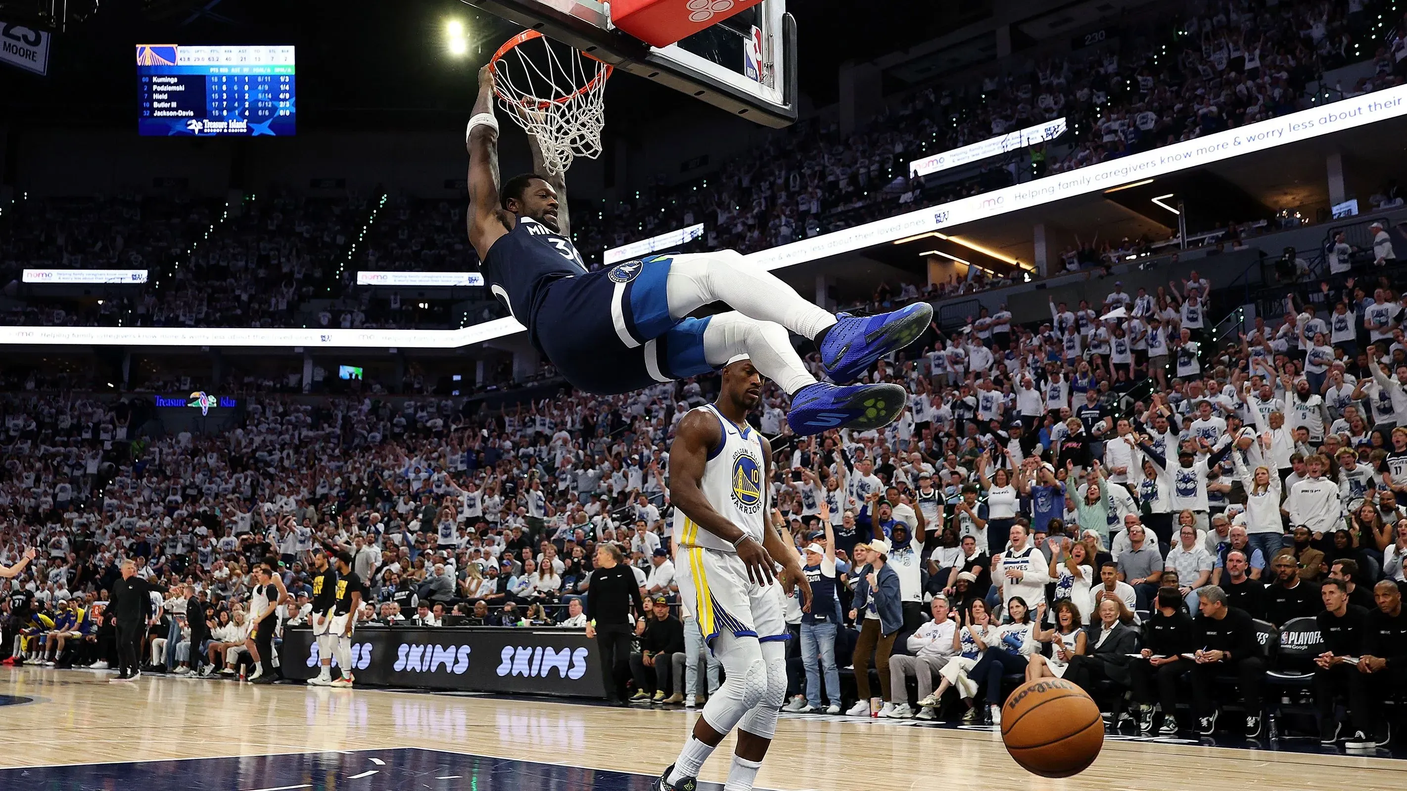 لاعب من فريق مينيسوتا تيمبروولفز يقوم بسلة مذهلة أثناء مباراة ضد جولدن ستيت ووريورز، مع جمهور متحمس في الخلفية.