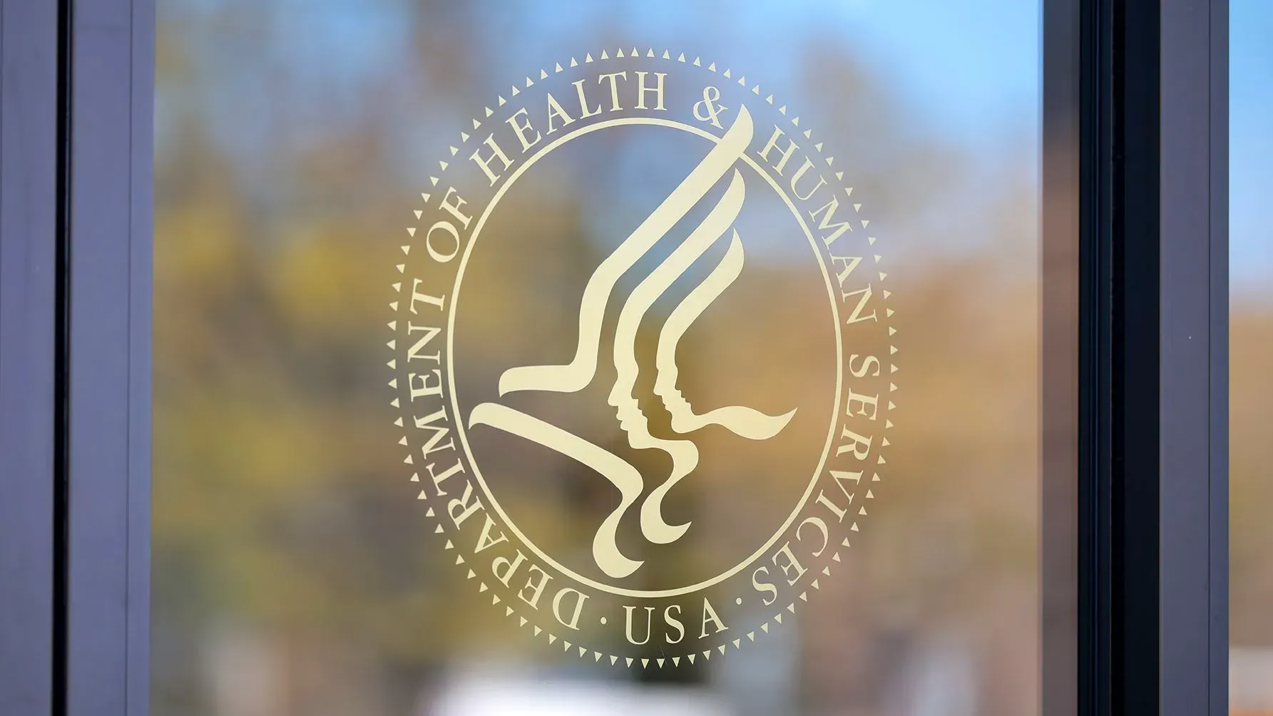 شعار وزارة الصحة والخدمات الإنسانية الأمريكية على نافذة، يرمز إلى الجدل حول إعادة هيكلة الوكالة وتأثيرها على برامج الصحة العامة.