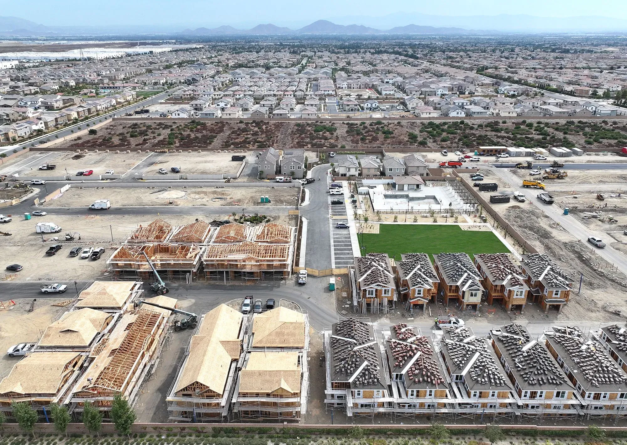مشهد جوي لحي سكني قيد الإنشاء، يظهر منازل جديدة في مراحل مختلفة من البناء، مع مناظر طبيعية محيطة ومنازل قائمة في الخلفية.