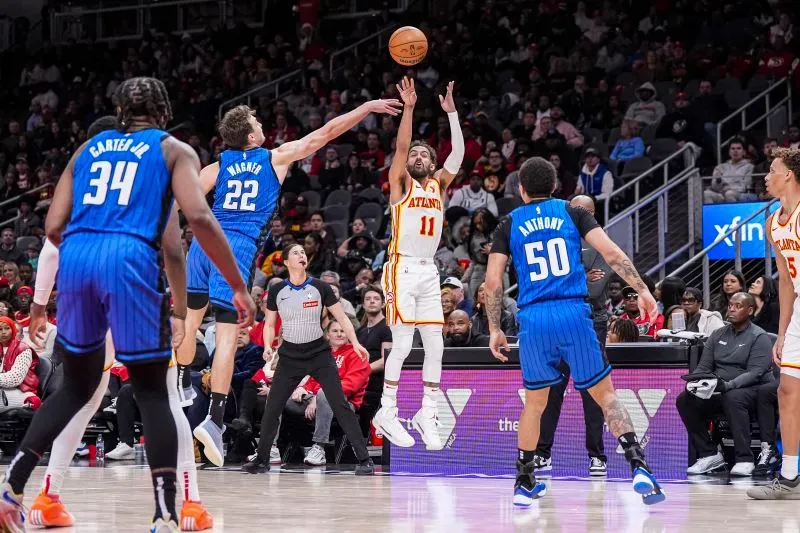 لاعب من أتلانتا هوكس يسدد كرة سلة بينما يحاول لاعب من أورلاندو ماجيك اعتراض التسديدة في مباراة مثيرة بالدوري الأمريكي للمحترفين.