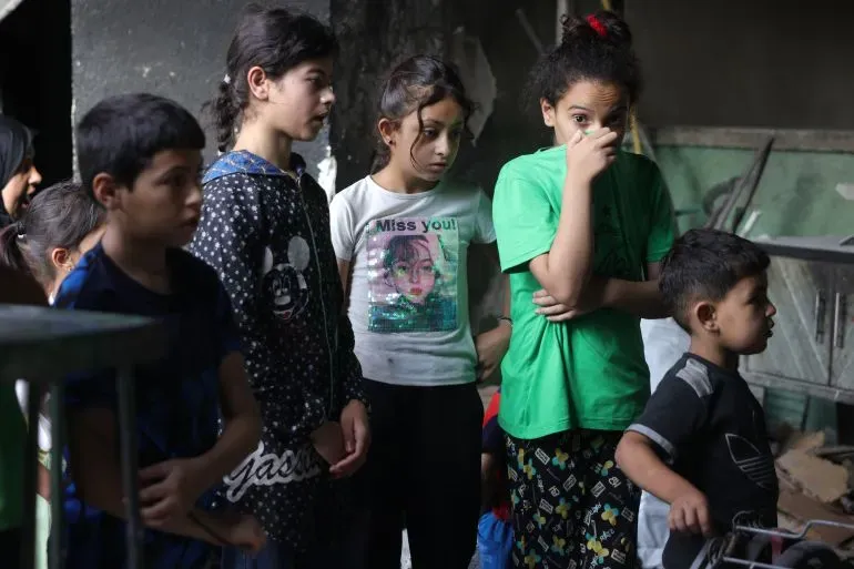 مجموعة من الأطفال في وضع حزين، يظهرون مشاعر القلق في بيئة تضررت من الصراع في فلسطين. تعكس الصورة الأزمة الإنسانية المستمرة.
