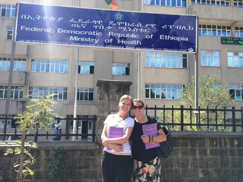 صورة للدكتورة مارجريت كاربنتر وصديقتها أمام وزارة الصحة الإثيوبية، حيث تساهمان في تقديم الرعاية الصحية وتعزيز حقوق الإجهاض.