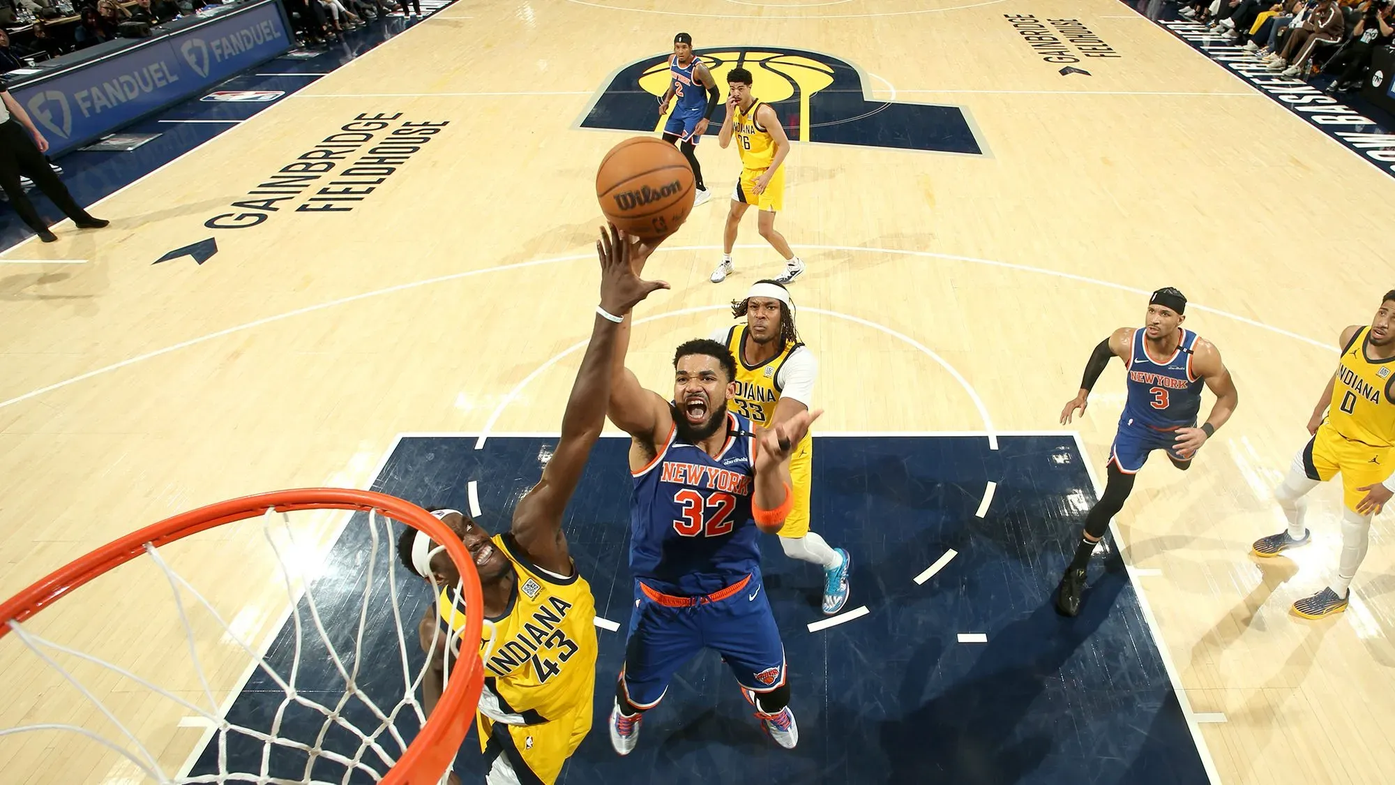 لاعب نيويورك نيكس كارل-أنثوني تاونز يسجل نقطة خلال مباراة حماسية ضد إنديانا بيسرز، مع تواجد لاعبين آخرين في الخلفية.