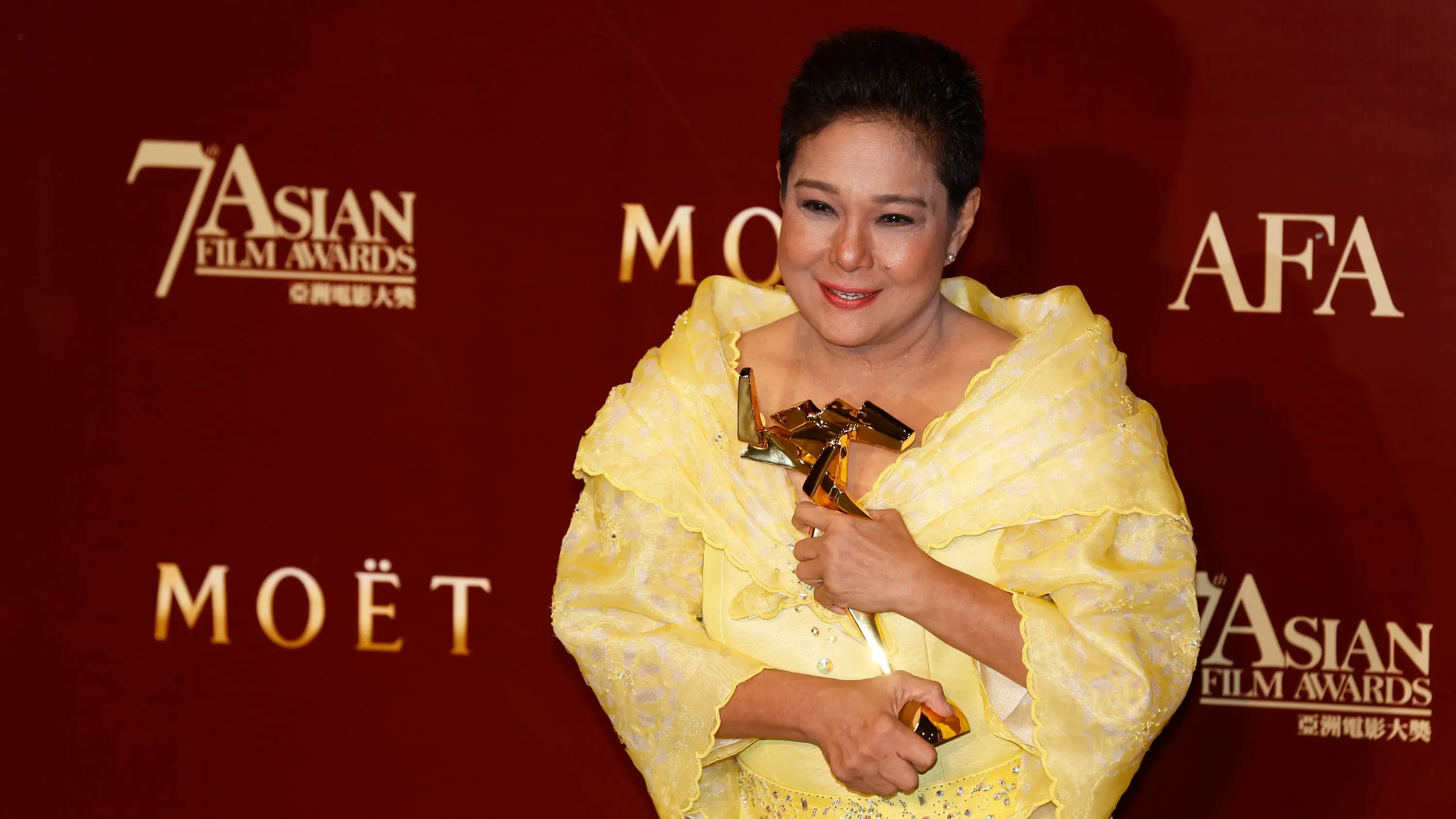 تظهر نورا أونور، نجمة السينما الفلبينية، بفستان أصفر وهي تحمل جائزة في حفل جوائز الأفلام الآسيوية، مع خلفية تحمل شعار الحدث.