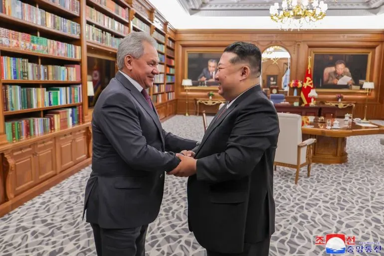 لقاء بين وزير الدفاع الروسي سيرغي شويغو والزعيم الكوري الشمالي كيم جونغ أون في مكتب مزين بالكتب، يعكس التعاون العسكري بين البلدين.