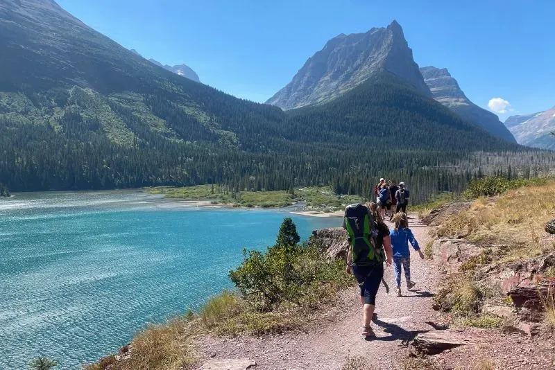 مجموعة من الأشخاص يسيرون على ممر بجوار بحيرة زرقاء، محاطة بالجبال الخضراء، مما يعكس جمال الطبيعة في منطقة نورث كونتري.