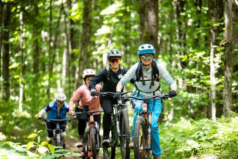 مجموعة من راكبي الدراجات الجبلية يستمتعون بتجربة ركوب الدراجات في غابة خضراء، مما يعكس جمال الطبيعة في منطقة نورث كونتري.