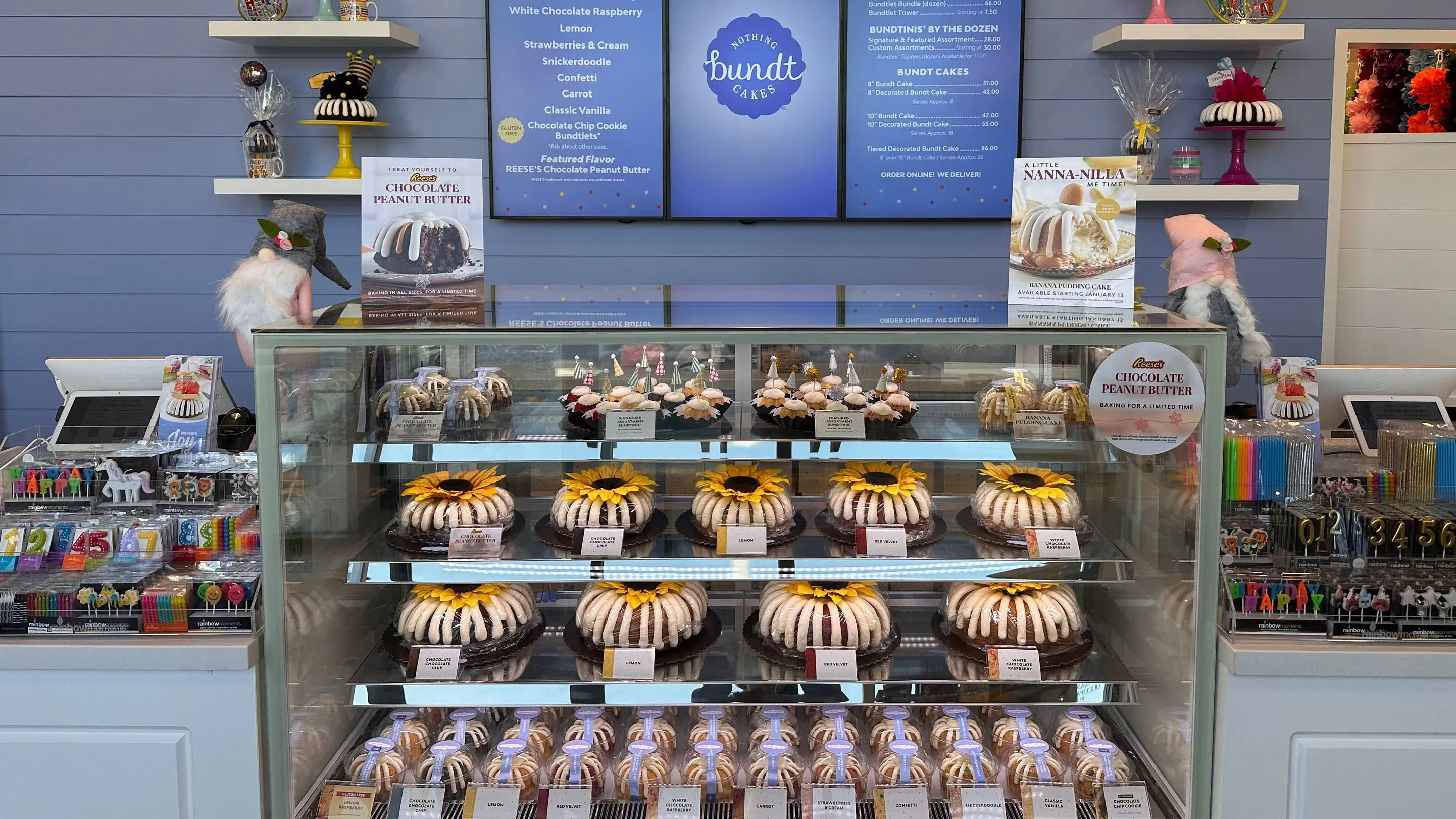 واجهة داخلية لمخبز "Nothing Bundt Cakes" تظهر مجموعة متنوعة من الكعك الملون بأحجام وتصاميم مختلفة، مع قائمة الأسعار في الخلف.