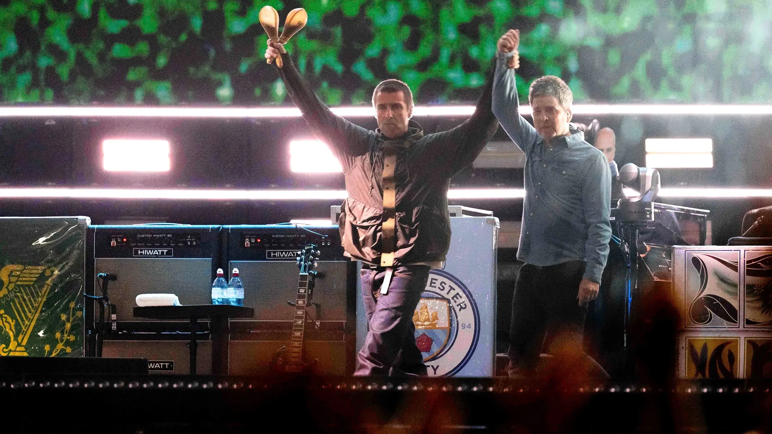 ليام ونويل غالاغر يرفعان أيديهما معًا على المسرح خلال حفل لم الشمل لفرقة Oasis في كارديف، بحضور جمهور حماسي.