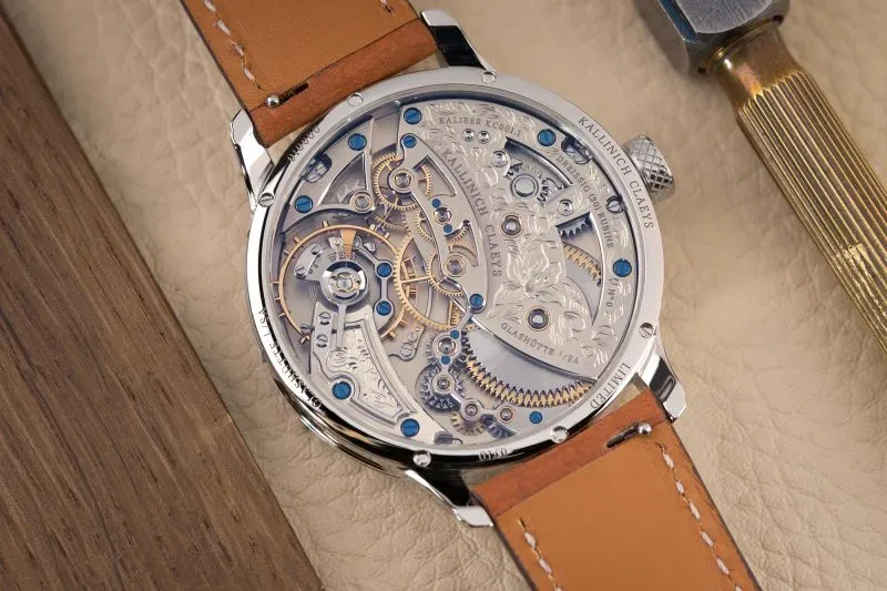 ساعة ميكانيكية تظهر تفاصيل آلية معقدة، مع حزام جلدي بني، محاطة بمواد خام، تعكس دقة صناعة الساعات التقليدية واهتمام الجيل الجديد.