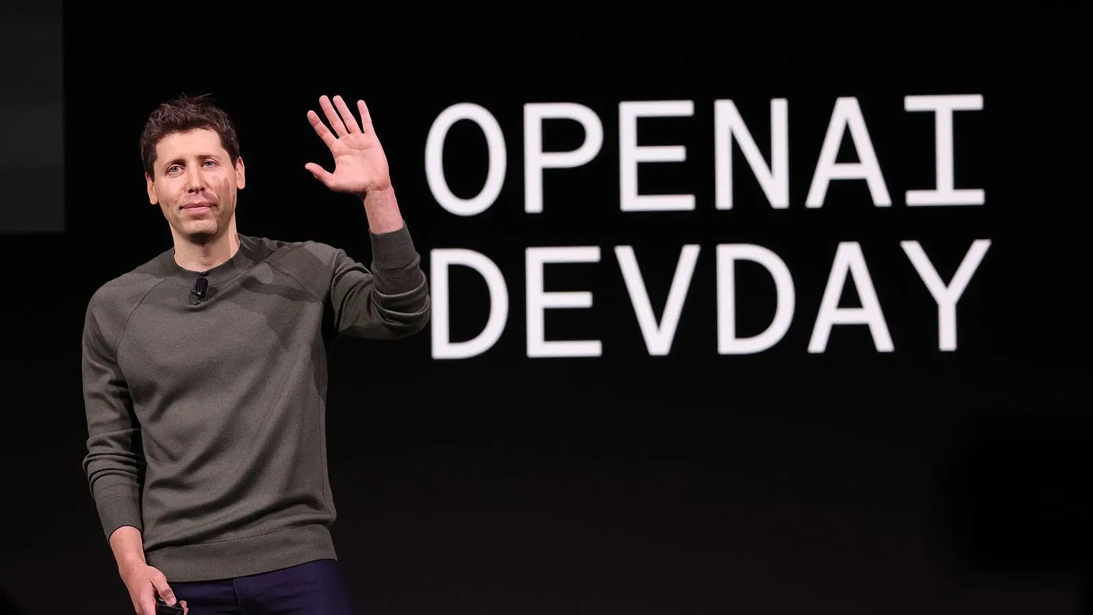 سام ألتمان، الرئيس التنفيذي لشركة OpenAI، يرحب بالحضور في حدث Dev Day، مع خلفية تحمل اسم الحدث.