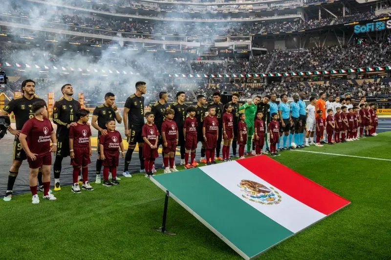 تشكيلة منتخب المكسيك الوطني لكرة القدم قبل مباراة في ملعب سوفي، مع العلم المكسيكي ووجود أطفال يحملون أعلامًا، وسط أجواء احتفالية.