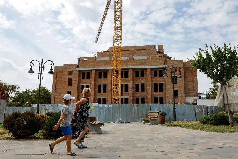 امرأتان تسيران بجوار موقع بناء في ماريوبول، حيث تظهر أعمال الترميم وسط دمار المدينة بعد الاحتلال الروسي.