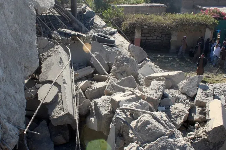 أنقاض مباني مدمرة في أفغانستان بعد غارات جوية باكستانية، مع وجود أشخاص في الخلفية يتفقدون الأضرار الناتجة عن الهجمات.