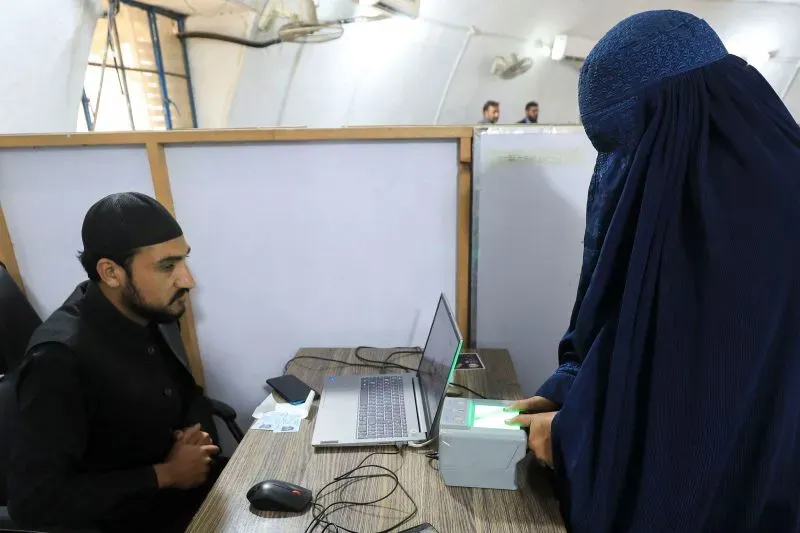 امرأة ترتدي البرقع تضع بصمتها على جهاز تسجيل بينما يجلس موظف أمام الكمبيوتر، في سياق إجراءات تسجيل اللاجئين الأفغان في باكستان.