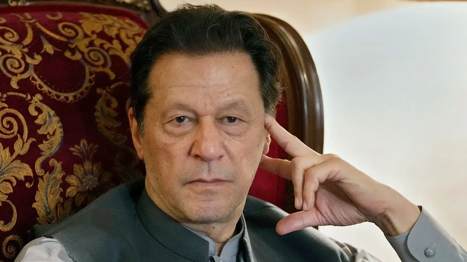 عمران خان، رئيس وزراء باكستان السابق، يجلس بتفكير عميق، مرتديًا ملابس رسمية، في خلفية فاخرة تعكس أجواء السلطة.