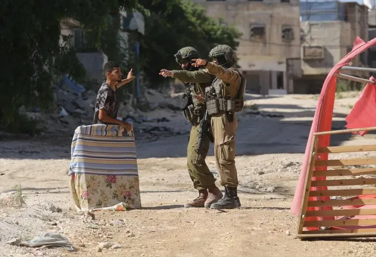 جنود إسرائيليون يوجهون أوامر لشاب فلسطيني مقيد اليدين في منطقة مسافر يطا، مما يعكس التوترات المتزايدة في الضفة الغربية.