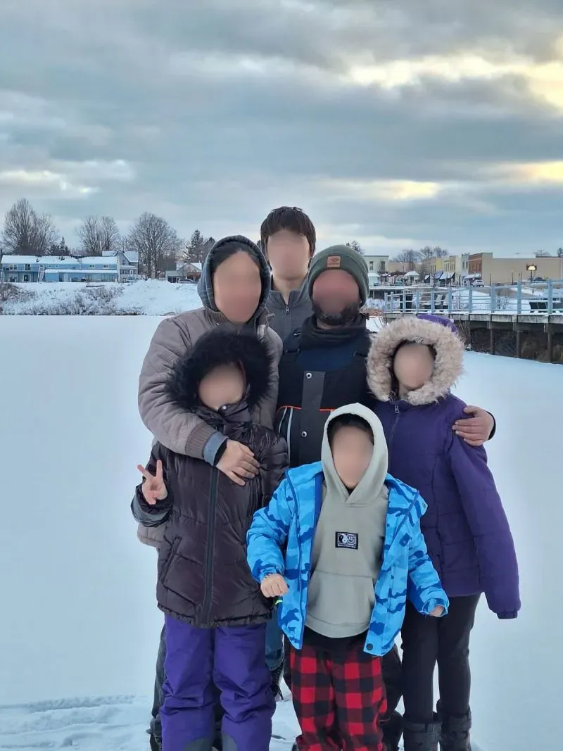 عائلة مكونة من ستة أفراد في منطقة ثلجية، حيث يحتضن الوالدان أطفالهم مع ارتداء ملابس شتوية، مع خلفية تضم سماء غائمة.