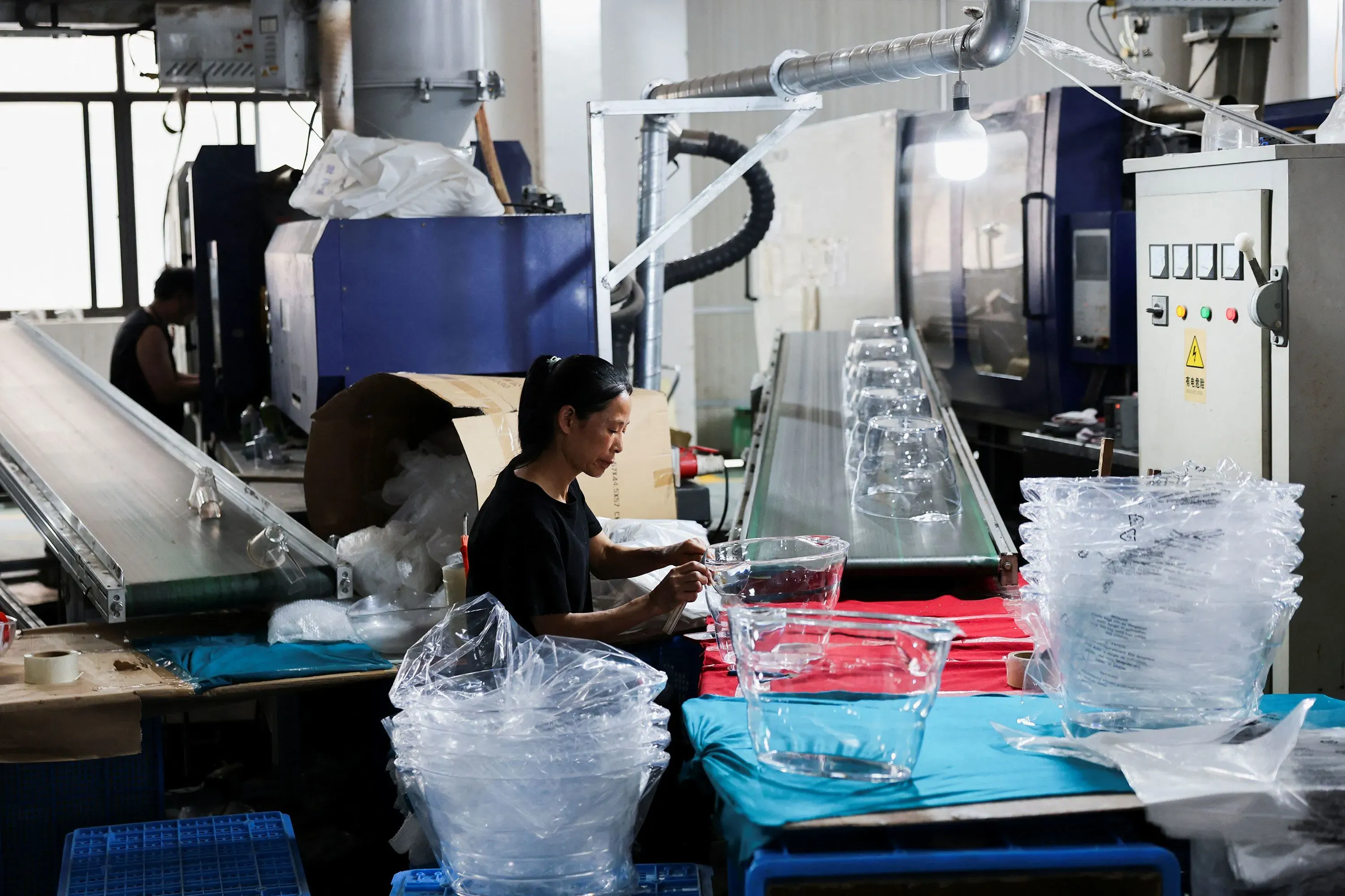 امرأة تعمل في مصنع لتصنيع المنتجات البلاستيكية، حيث تظهر آلات الإنتاج وأدوات التعبئة والتغليف، مما يعكس تأثير ارتفاع أسعار النفط على السوق.