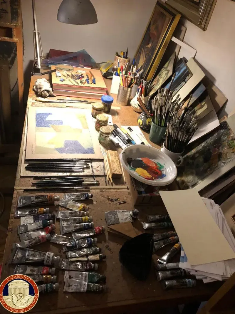 طاولة فنية تحتوي على أنابيب طلاء وأدوات رسم، تُظهر ورشة عمل تُستخدم في إنتاج لوحات فنية مزورة في روما.