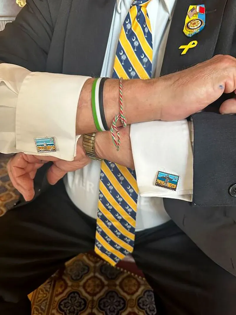 أزرار أكمام تحمل رموزًا أوكرانية، مع أساور ملونة، تعكس دعم النائب مايكل ماكول لأوكرانيا في سياق النقاشات السياسية حول الحرب.