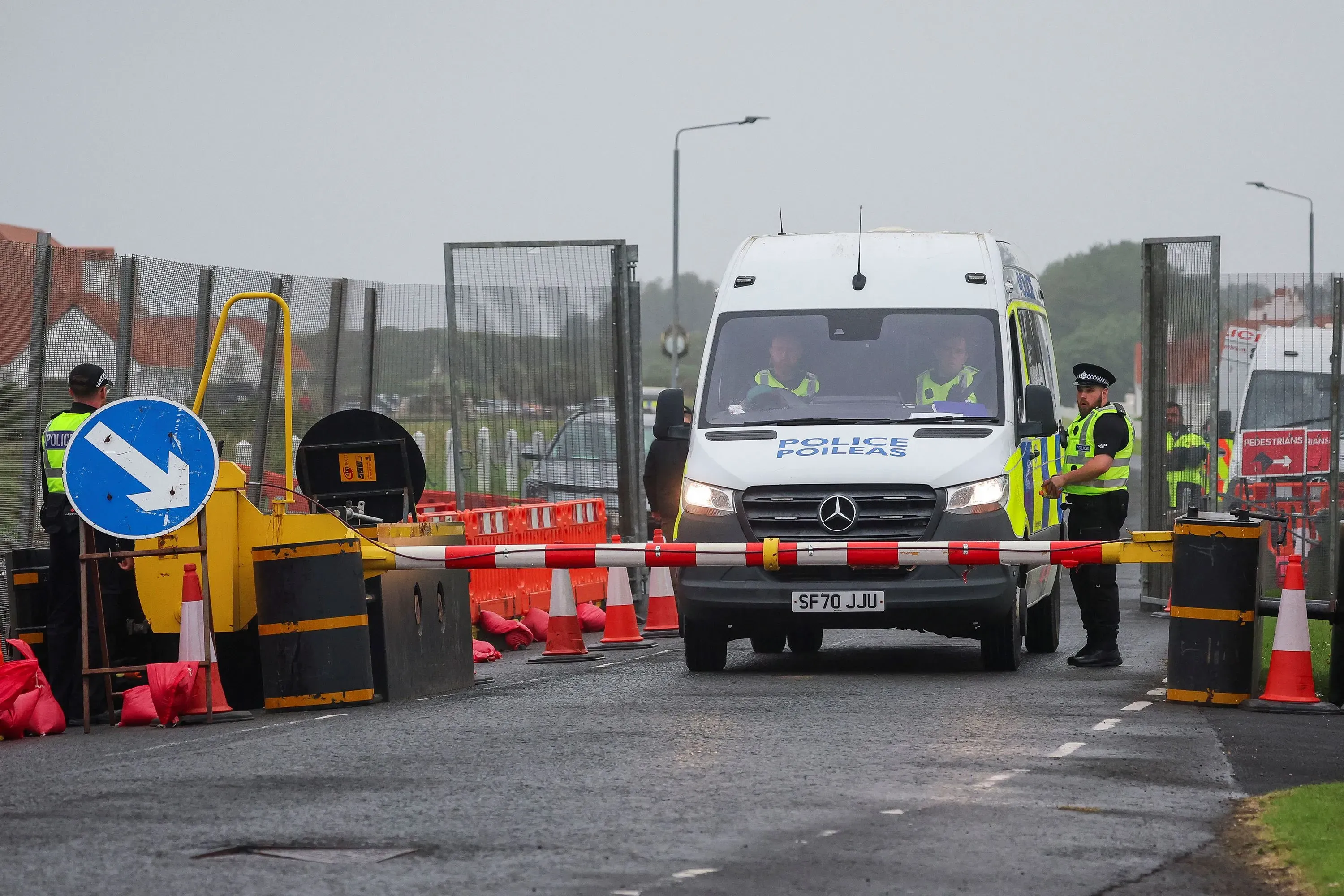 حواجز أمنية وشرطة في موقع زيارة ترامب إلى اسكتلندا، مع وجود مركبة شرطة ومجموعة من رجال الشرطة في الخلفية.
