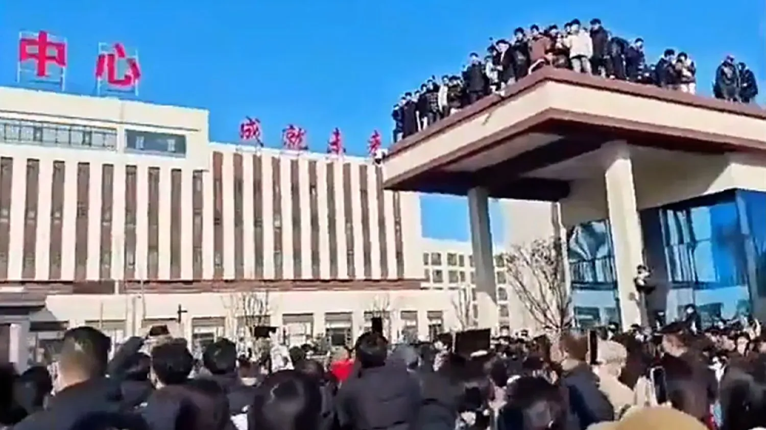 احتجاجات في مدرسة بوتشنغ التقنية في الصين، حيث يتجمع حشد كبير من الطلاب أمام الشرطة، مع وجود متظاهرين على السطح.