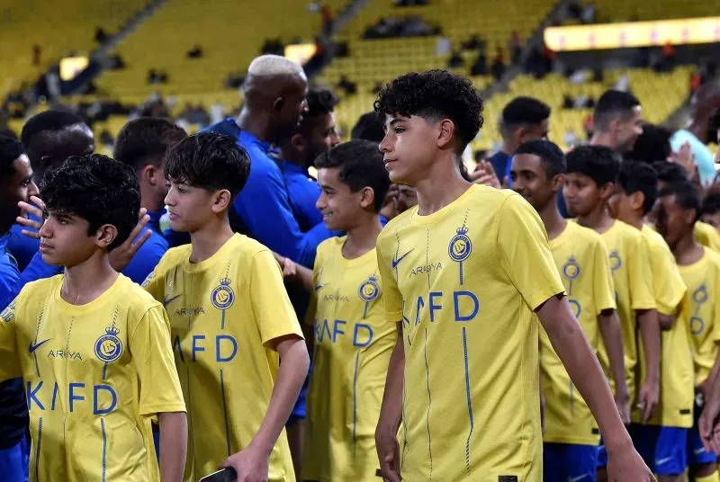 رونالدو جونيور، لاعب نادي النصر السعودي، يرتدي زي الفريق الأصفر أثناء التحية قبل مباراة، مع زملائه في الفريق.
