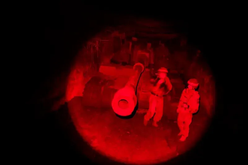 جنود أوكرانيون يقفون بجانب مدفع في موقع عسكري مضاء باللون الأحمر، مما يعكس الأجواء المشحونة في الصراع.