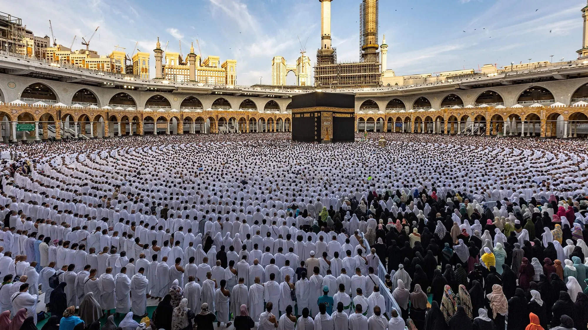 مصلون يرتدون ملابس بيضاء وسوداء في ساحة الحرم المكي، حيث يتجمعون حول الكعبة استعدادًا لشهر رمضان.
