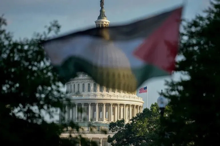 علم فلسطيني يرفرف أمام مبنى الكابيتول الأمريكي، مع العلم الأمريكي في الخلفية، مما يرمز إلى الجدل حول الدعم العسكري لإسرائيل.