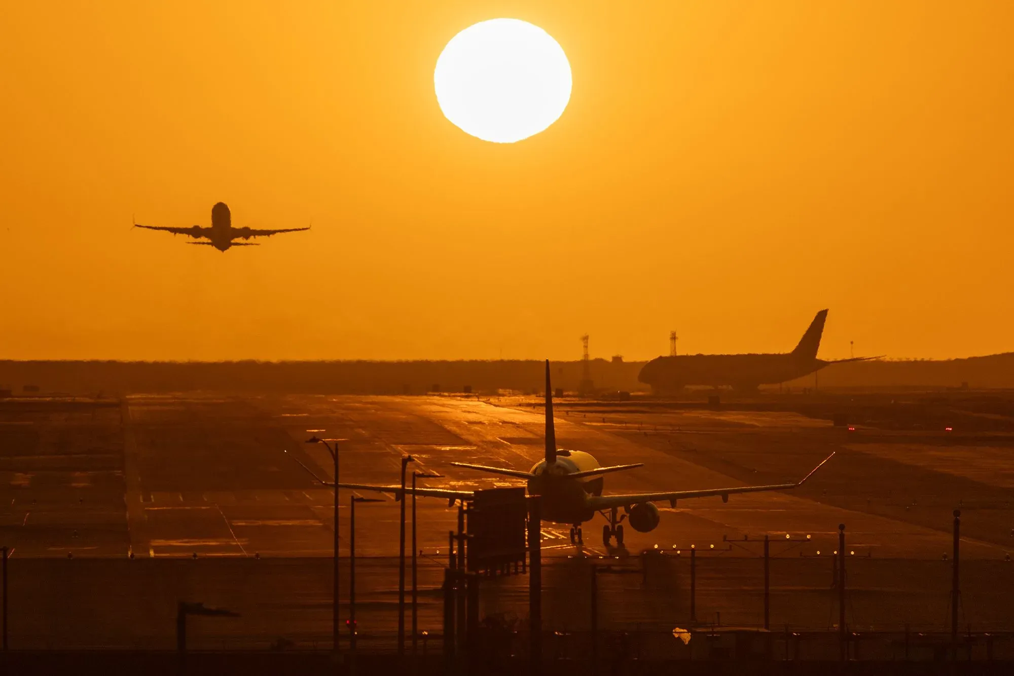 طائرة تقلع تحت شمس غاربة، مع طائرات أخرى متوقفة على المدرج، تعكس تأثير نقص وقود الطائرات على السفر الجوي.