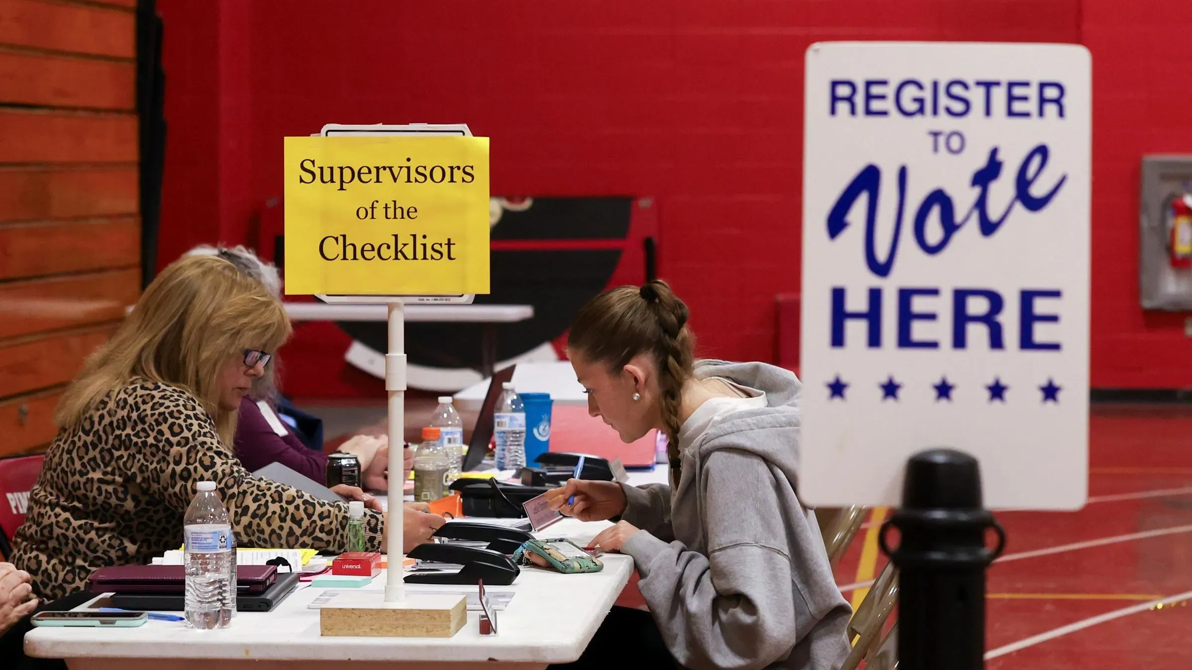 مكتب تسجيل الناخبين يظهر موظفين يعملون على التحقق من الوثائق مع لافتة تشير إلى ضرورة التسجيل للتصويت، في سياق جهود إثبات الجنسية.