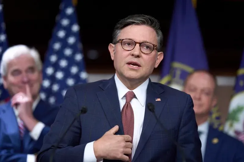 رجل يتحدث في مؤتمر صحفي، مع أعلام خلفه، يناقش تأثير تصريحات إيلون ماسك على التشريع الأمريكي.