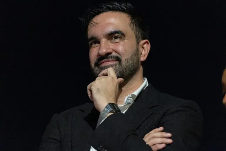 زهران ممداني، عمدة مدينة نيويورك الجديد، يظهر مبتسمًا أثناء حديثه، محاطًا بأجواء من التوتر السياسي حول جنسيته.