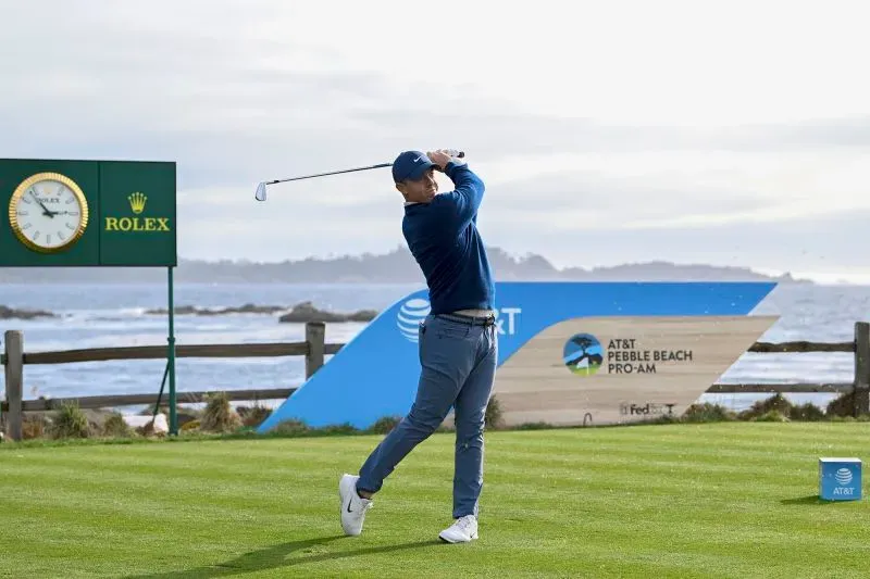 روري ماكلروي يسدد ضربة جولف في بطولة بيبل بيتش، مع وجود لافتة للبطولة في الخلفية، تعكس أجواء المنافسة على الساحل.