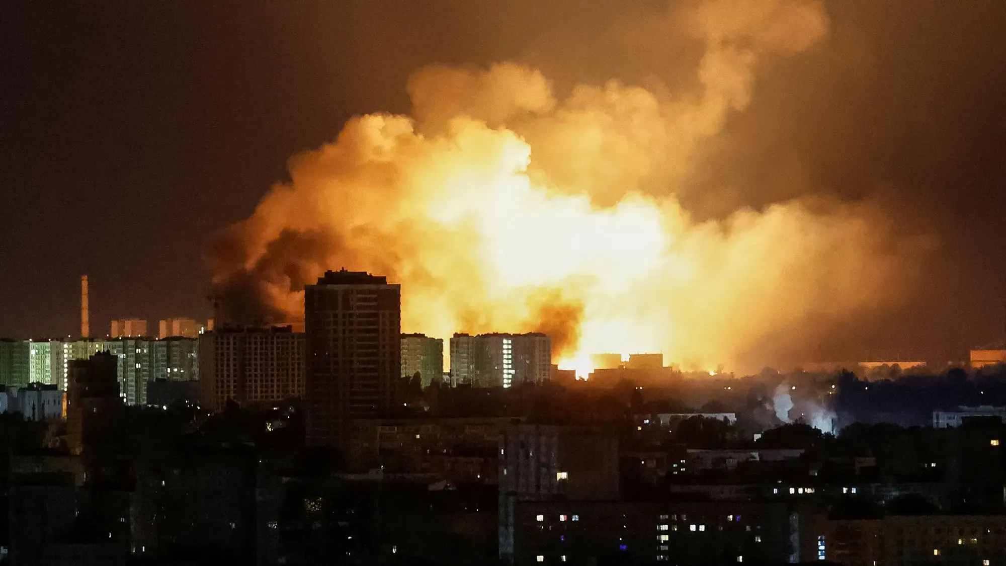 انفجارات ضخمة تضيء سماء مدينة أوكرانية ليلاً، مع تصاعد الدخان الكثيف من المباني، مما يعكس تصاعد التوترات في الصراع الأوكراني الروسي.