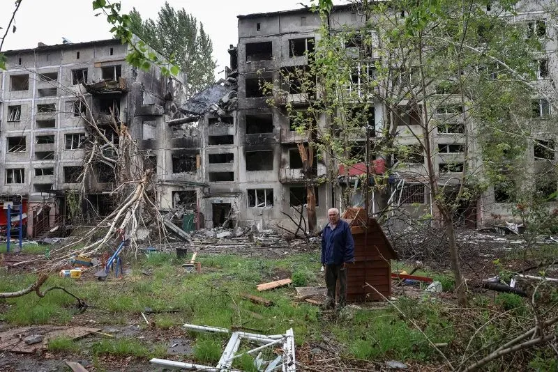 رجل مسن يقف أمام مبنى سكني مدمر في منطقة تأثرت بالصراع، مما يعكس آثار الحرب المستمرة بين روسيا وأوكرانيا.