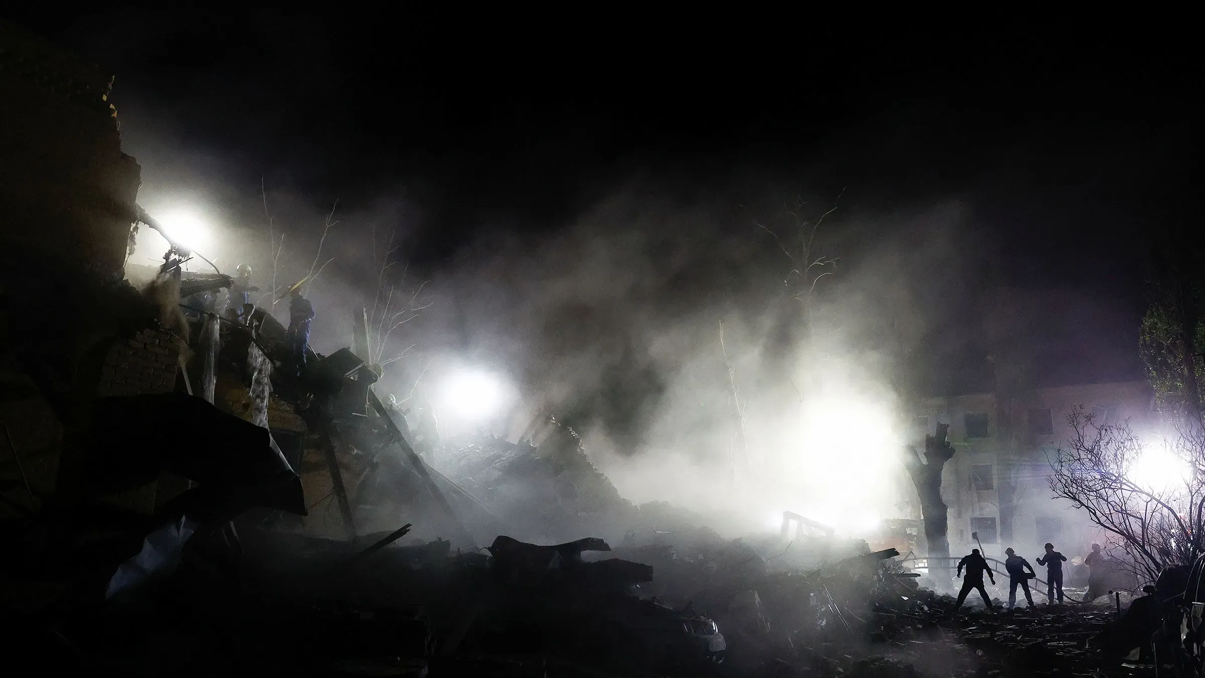 تظهر الصورة فرق الإنقاذ تعمل تحت الأضواء الساطعة وسط الدخان والأنقاض، بعد الهجمات الروسية على كييف، مما يعكس حالة الطوارئ والمأساة.