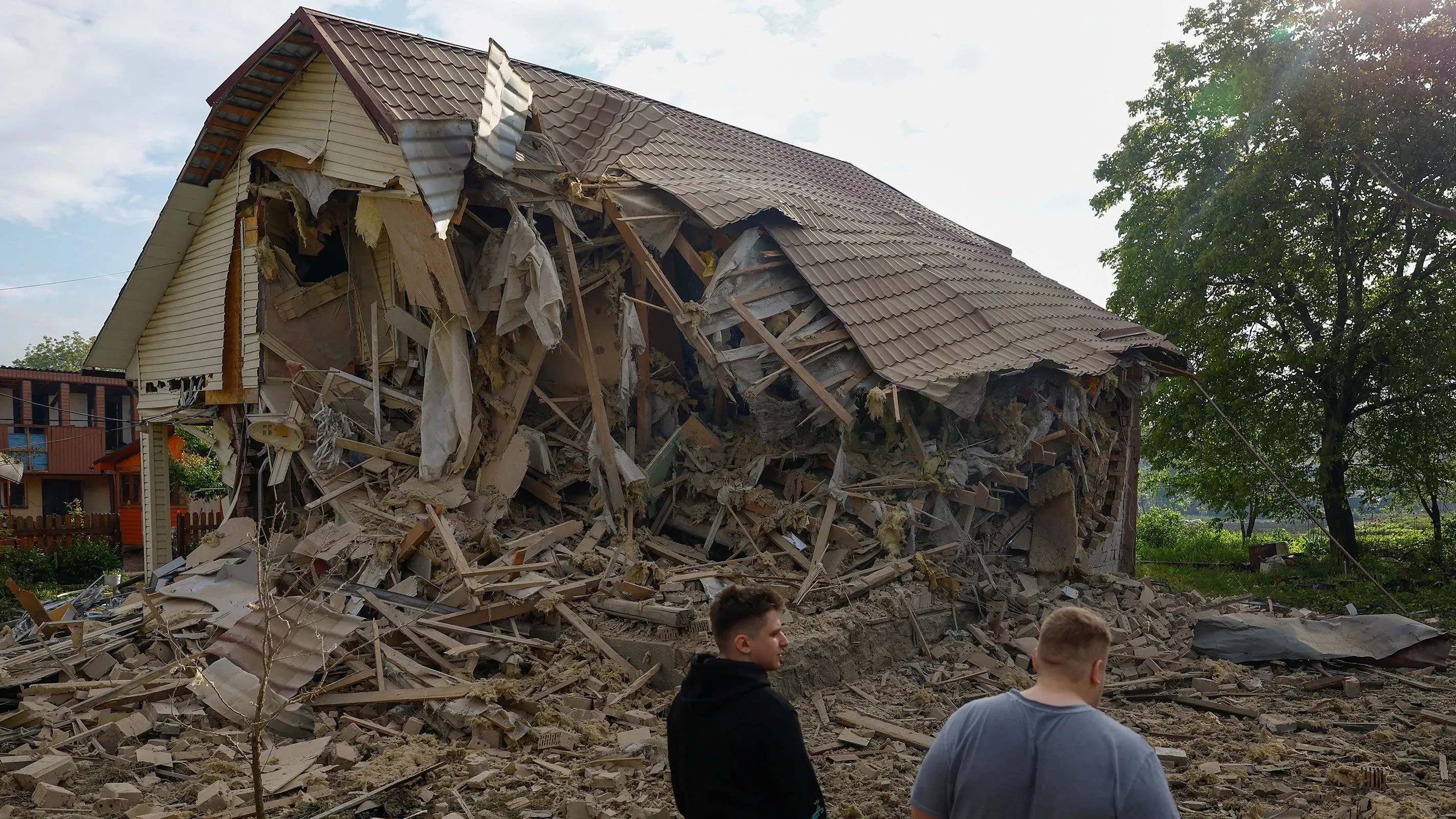 منزل مدمر جراء هجوم بطائرات مسيرة روسية في أوكرانيا، مع وجود شخصين يتفقدان الأضرار في الموقع.