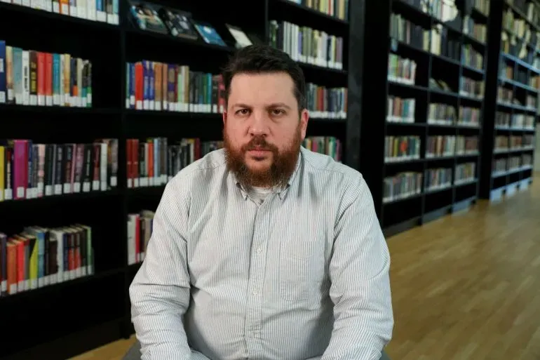 ليويد فولكوف، المعارض الروسي، يجلس في مكتبة، خلفه رفوف مليئة بالكتب، بعد الحكم عليه بالسجن لمدة 18 عامًا بتهم سياسية.