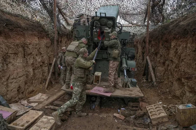 جنود أوكرانيون يعملون على تحميل مدفع في خندق، مع وجود معدات عسكرية في الخلفية، مما يعكس الأجواء القتالية في ساحة المعركة.