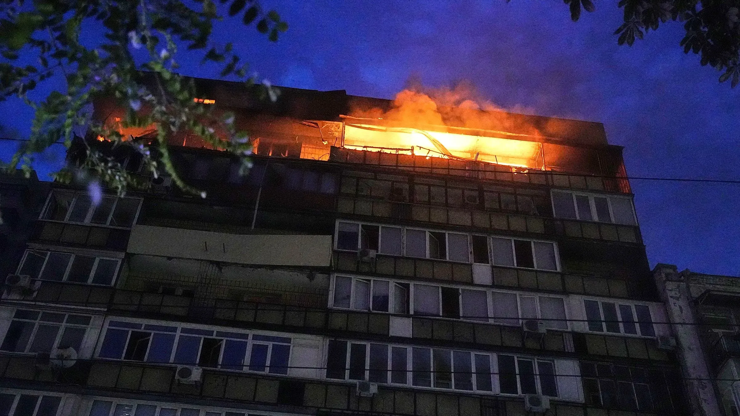 الحرائق تشتعل في مبنى سكني في كييف بعد هجوم جوي روسي، مع تصاعد الدخان في السماء الزرقاء، مما يعكس الأضرار الكبيرة الناتجة عن القصف.