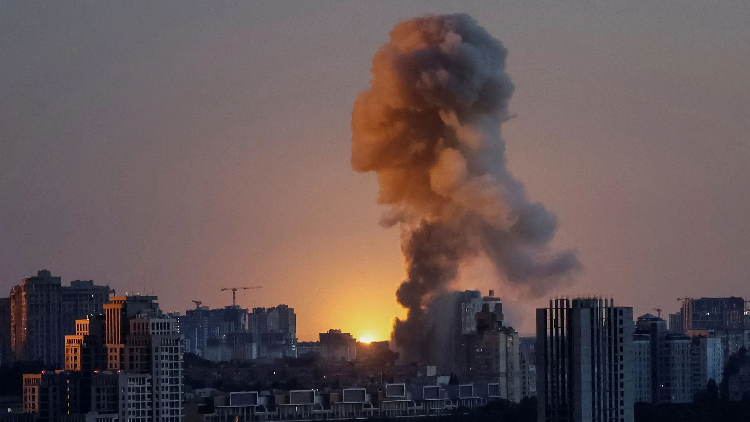 دخان يتصاعد من انفجار في كييف عند غروب الشمس، مع مبانٍ سكنية في الخلفية، مما يعكس تصاعد التوترات في الصراع الأوكراني.